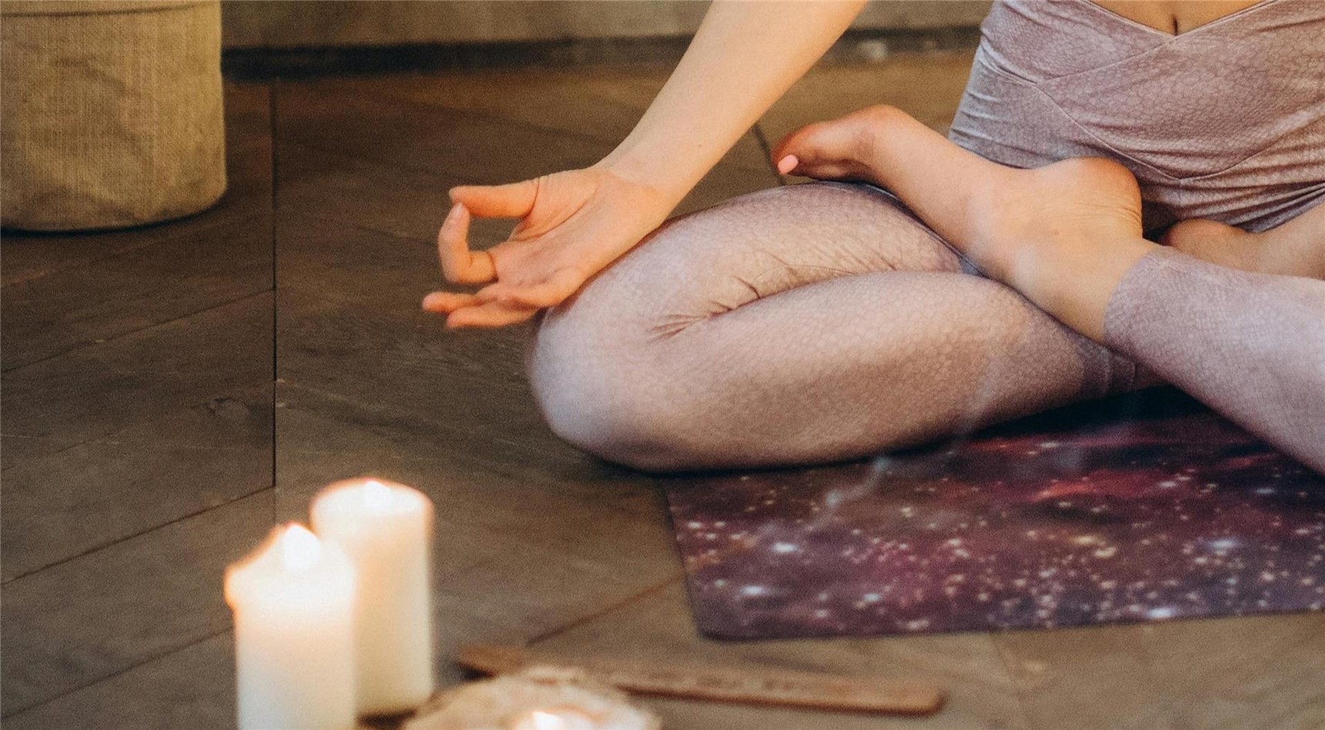 Eine Frau in Yoga-Leggings sitzt auf dem Boden, umgeben von brennenden Kerzen.
