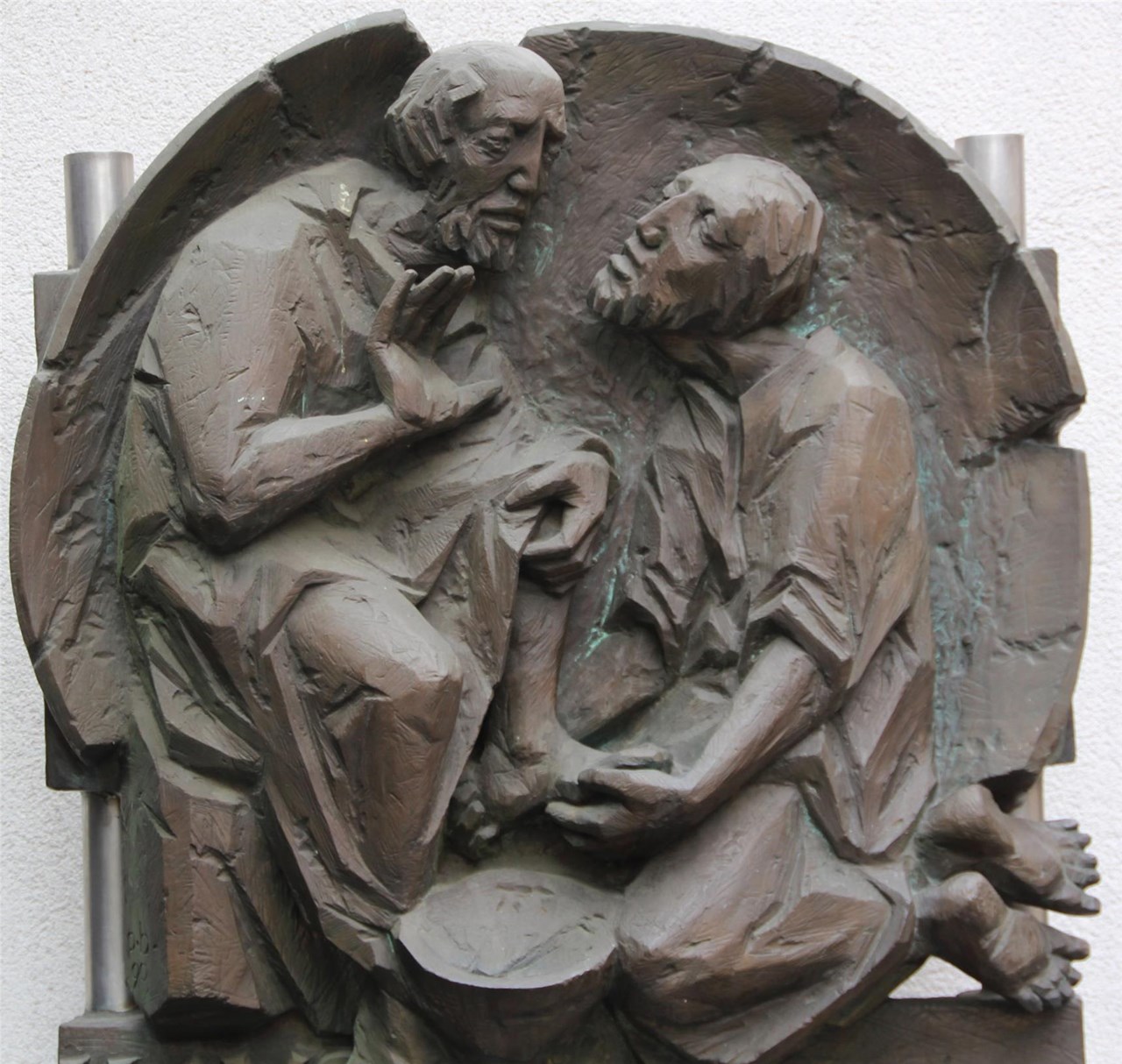 Eine bronzene Skulptur von zwei Männern. Ein Mann wäscht dem anderen die Füße.
