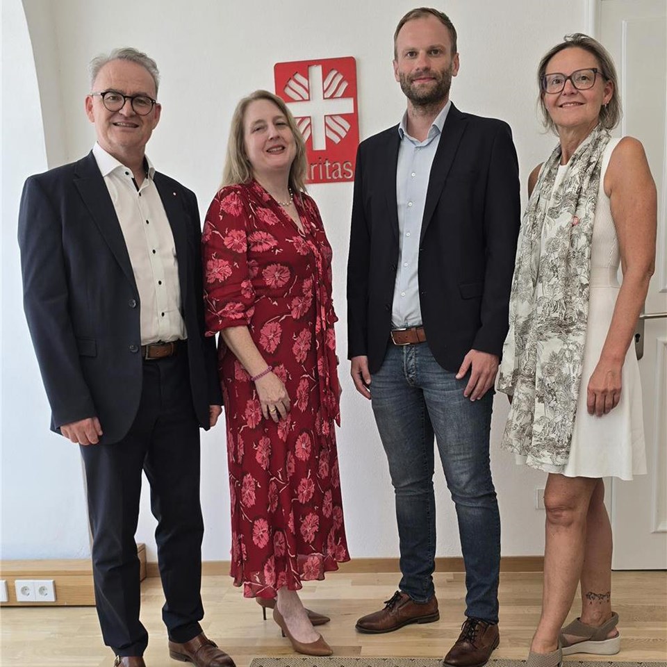 Vier Personen stehen in einem hellen Büroraum vor dem Caritas-Logo. Zu sehen sind Stefan Seiderer, Miriam Biber, Thomas Furthmeier und Andrea Anderlik.