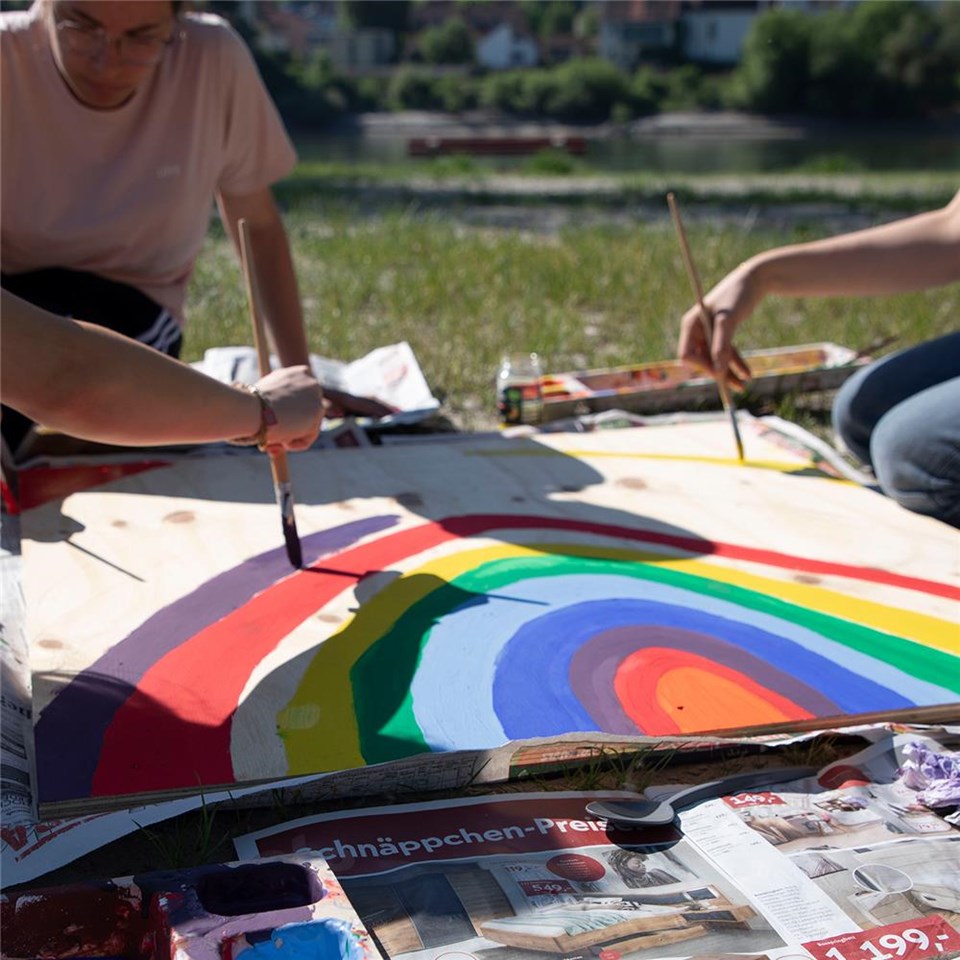 Drei Jugendliche malen einen Regenbogen auf ein Plakat.
