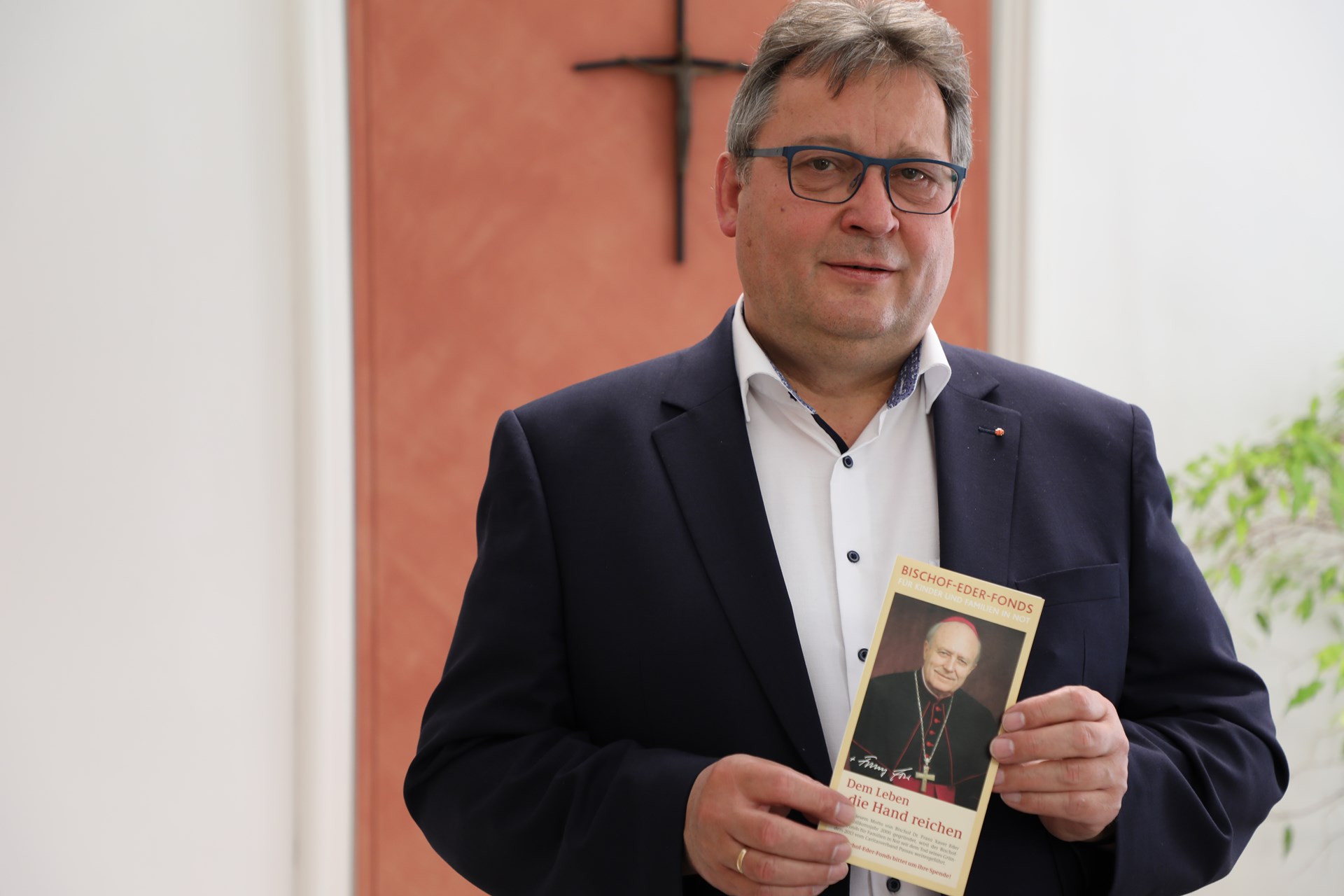 Caritasvorstand Konrad Niederländer hält einen Flyer mit dem Abbild von Bischof Eder in der Hand