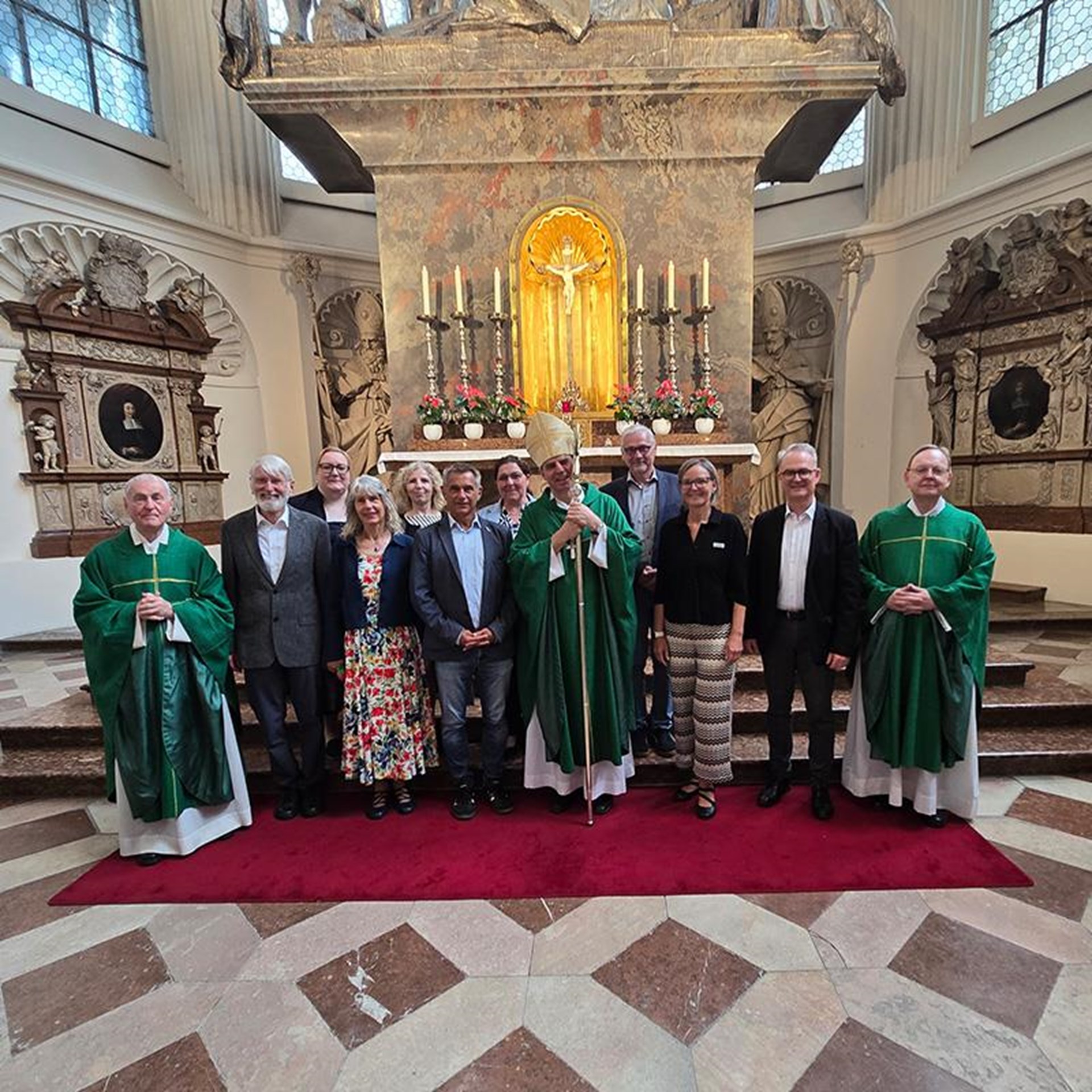 auf dem Bild ist eine Gruppe von Frauen und Männern zu sehen welche in einer Kirche vor dem Altar stehen. In der Mitte steht der Bischof. 