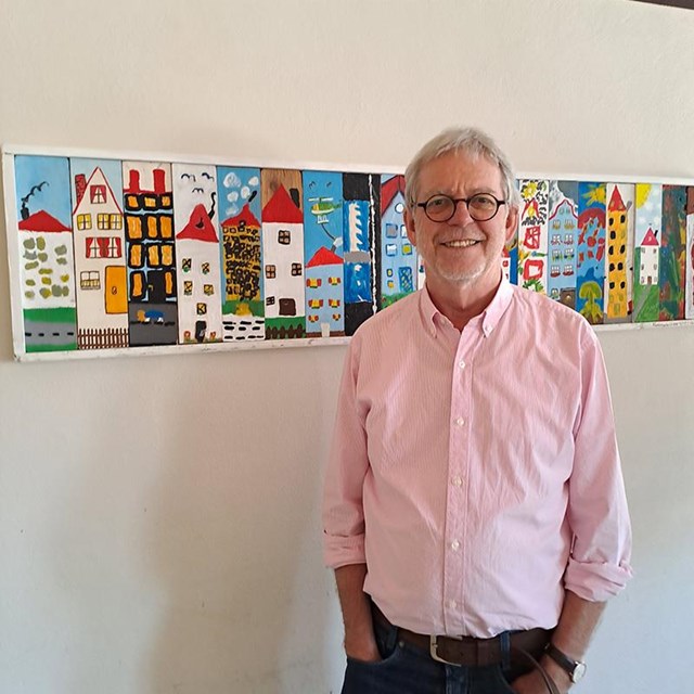 auf dem Bild ist ein Herr zu sehen im Hintergrund ist ein langes buntes Bild