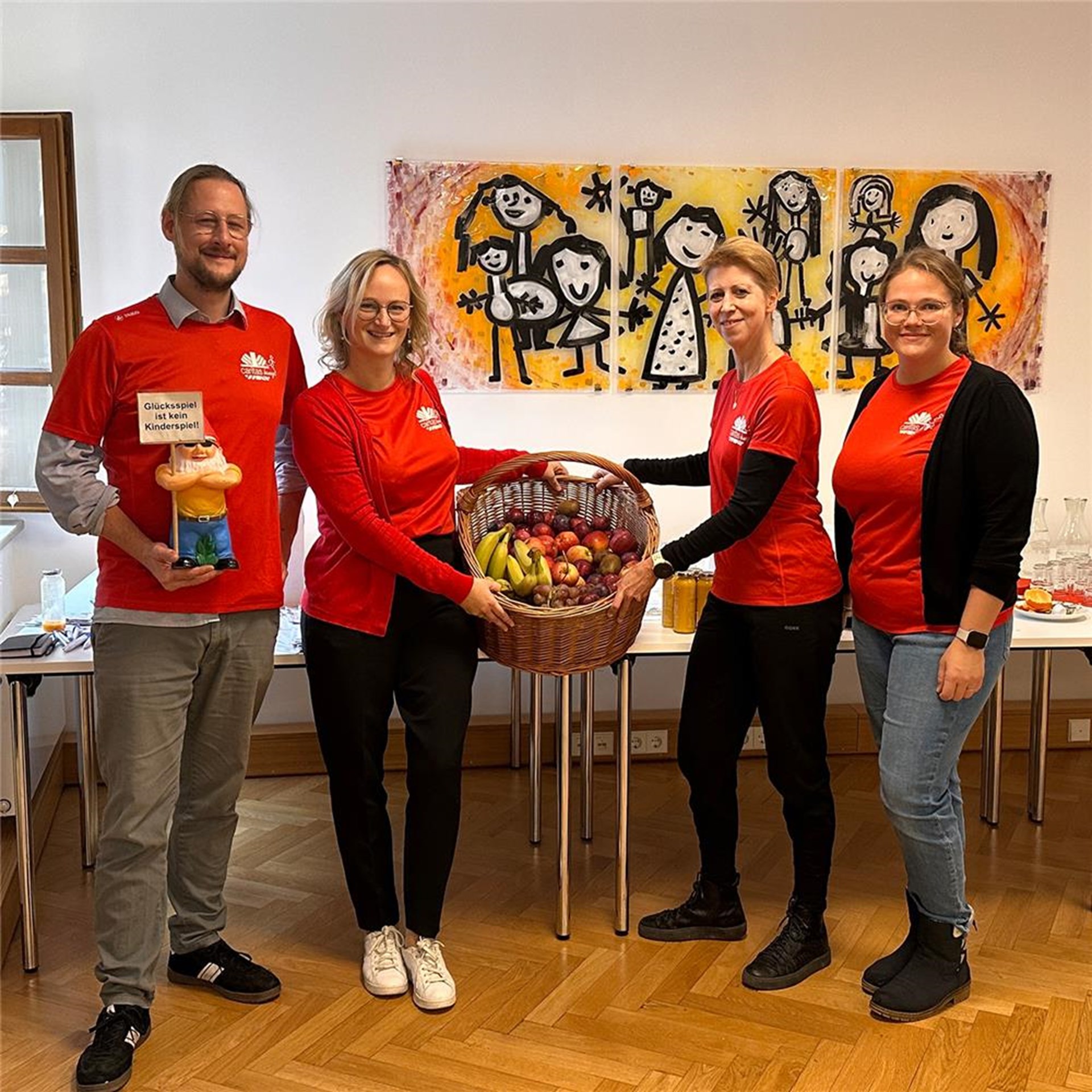 Vier Personen stehen vor einem Tisch mit Obst und Smoothies. Zwei Personen halten einen Korb voller Obst in der Hand.